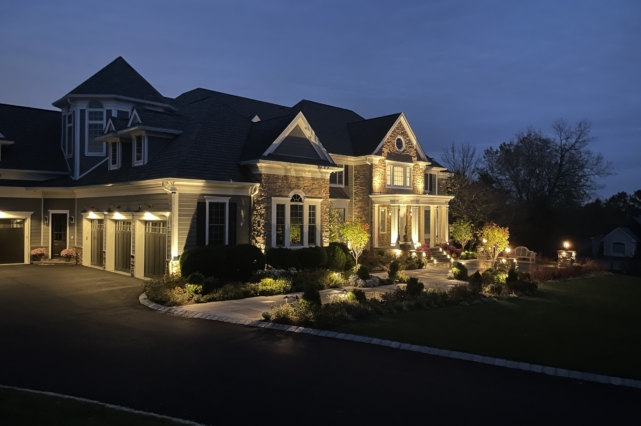 Image of a large home in the evening being spotlighted by warm outdoor lights