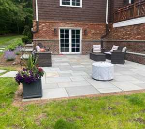 Backyard featuring a stone patio and walkway with chairs and plant pots