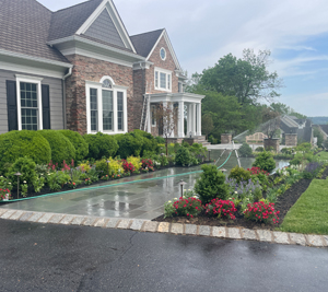 A front walkway to a large stone home surrounded by bushes, flowers, and other plants on each side 