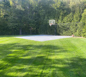 A lush green lawn that was just mowed with a basketball court in the background